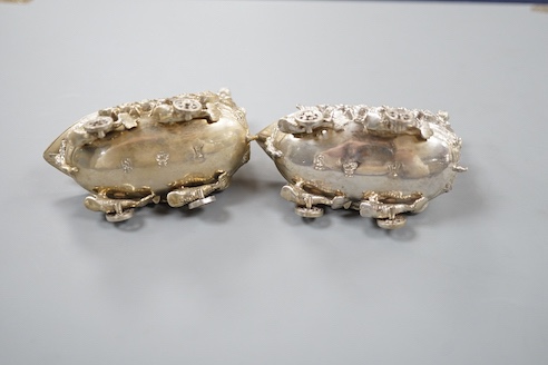 A pair of late 19th/early 20th century Hanau white metal salts, modelled as boat's with wheels and putti surmounts, maker Stork & Sinsheimer, length 81mm, 195 grams.